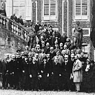 Schwarzweißfoto einer großen Gruppe von Männern in franziskanischen Habit und bürgerlicher Kleidung, versammelt auf einer Außentreppe vor einem historischen Gebäude; einige sitzen, die meisten stehen, ernste Mienen.