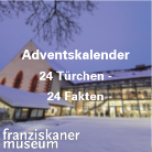 Franziskanermuseum mit markantem spitzem Dach, beleuchteter Glasfront und Schnee im Vordergrund bei Dämmerung; weiße Schrift: Adventskalender – 24 Türchen, 24 Fakten.