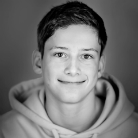 Schwarzweiß-Porträt eines jungen Mannes mit kurzem Haar und leichtem Lächeln, frontal, er trägt einen Kapuzenpullover vor unscharfem neutralem Hintergrund