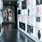 Moderner Museumsgang des Franziskanermuseums mit einer beleuchteten Wand aus rechteckigen Vitrinen rechts, darin Fotos, Schriftzeichen und Illustrationen; am Ende Ausstellungsraum mit Vitrine