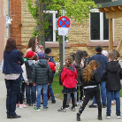 Gruppe von Kindern und Erwachsenen vor einem Backsteingebäude, eine Begleiterin erklärt etwas.