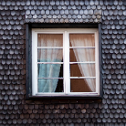 Weiß gerahmtes viergeteiltes Fenster mit halbgeschlossenen Gardinen in einer Fassade aus geschuppten Holzschindeln