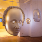 Drei großformatige, weiße, frei hängende Gesichtsskulpturen mit leuchtenden Augen in einem hellen Ausstellungsraum des Franziskanermuseums Villingen‑Schwenningen