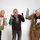Drei kostümierte Erwachsene vor weißem Hintergrund: links Mann mit Handpuppe, Mitte Mann mit roter Clownnase und zwei Puppen, rechts in braunem Gewand mit weißer Maskenpuppe.