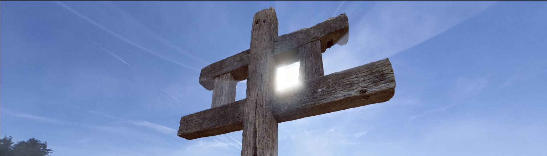 Weathered wooden Franciscan Tau cross viewed from below, sunlight streaming through its central opening against a clear blue sky