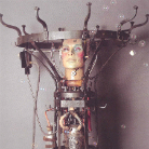 Mechanische Automatenfigur: bemalter menschlicher Kopf auf offenem Metallgestell mit Zahnrädern, Drähten, Vakuumröhren und Glaskolben; industriell-kurioses Ausstellungsobjekt