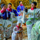 Gruppe traditionell kostümierter Fasnachtsfiguren mit geschnitzten Holzmasken, bunten Gewändern und Besen oder Stöcken, teils knieend, vor herbstlicher Baumkulisse