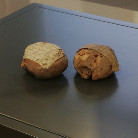 Zwei runde, dunkelbraune Brote mit gerissener Kruste als Ausstellungsobjekte auf einer dunklen Präsentationsfläche im Franziskanermuseum