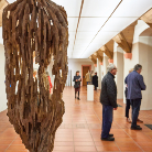 Innenansicht des Franziskanermuseums: Besucher betrachten an der Wand gezeigte Kunst, im Vordergrund eine große hängende Skulptur aus verwachsenen Holzstämmen; heller Ausstellungsraum mit Fliesenboden und sichtbaren Deckenbalken.