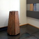 Kegelförmiges, hohles Holzgefäß aus senkrechten Bohlen mit dunkler Patina und Rissen, steht freistehend auf dem Boden im Ausstellungsraum des Franziskanermuseums.