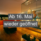 Warm beleuchteter Ausstellungsraum des Franziskanermuseums mit Glasvitrinen und ausgestellten Objekten; darüber Textbanner: Ab 16. Mai wieder geöffnet.