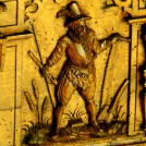 Goldfarbenes Metallrelief eines gehenden Pilgers mit breitkrempigem Hut, Umhang und Pilgerstab vor architektonischem Hintergrund