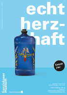 Blau glasierte hohe Flasche mit farbigen Blumen- und Rankenornamenten auf hellem türkisblauen Hintergrund; große weiße Schrift mit den Worten echt herzhaft im Hintergrund