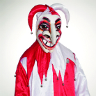 Person in rot-weißem Narrenkostüm mit spitzem Glockenhut und einer übergroßen, weiß-rot bemalten Maske mit breitem Grinsen, hohem Stirnansatz, betonten Augenpartien und langer spitzer Nase